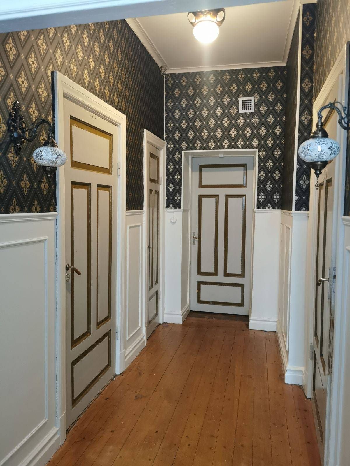 Hall med mönstrad tapet, spegeldörrar och trägolv